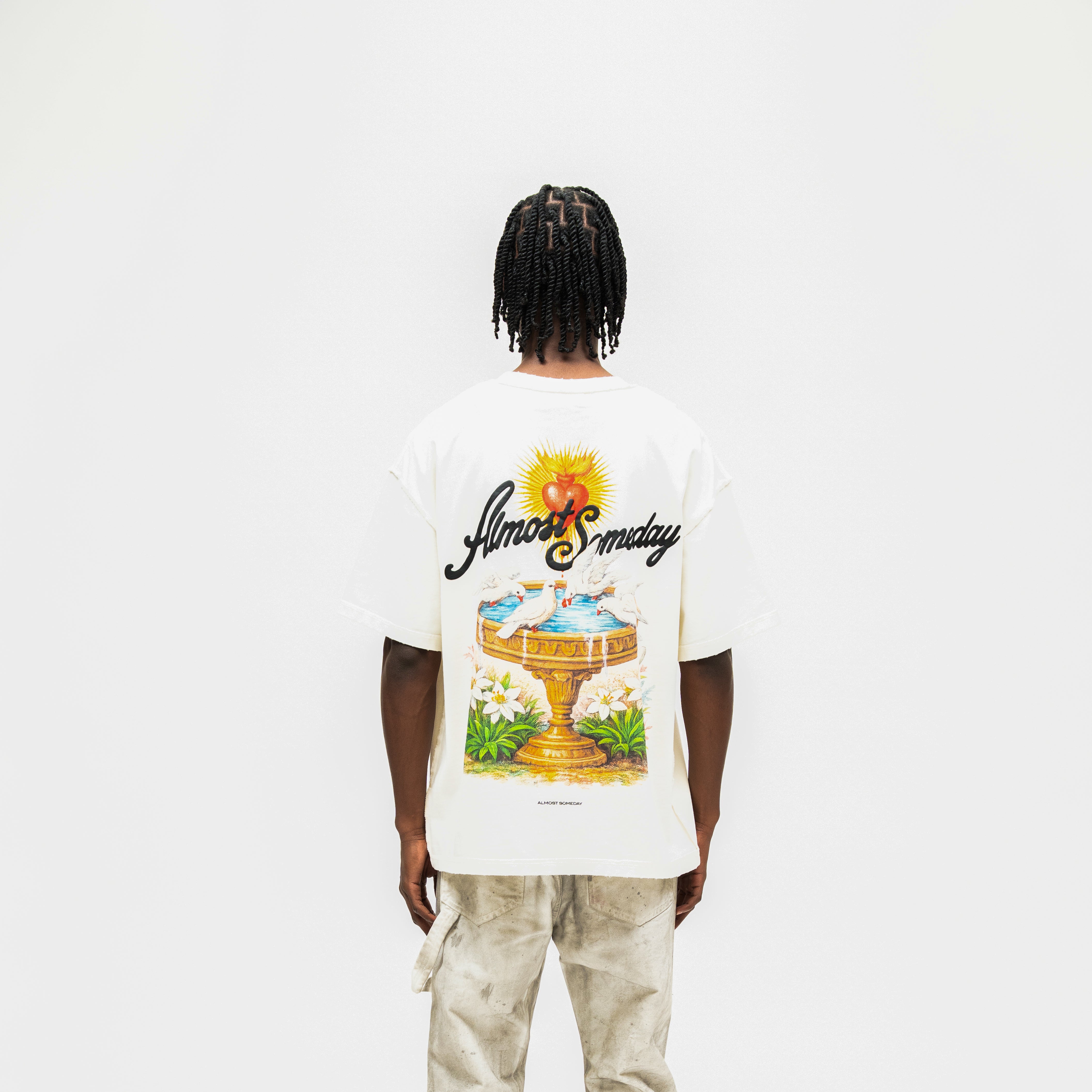 Fountain Tee – Cream – Back view on model showing fountain, doves, flowers, and ALMOST SOMEDAY lettering