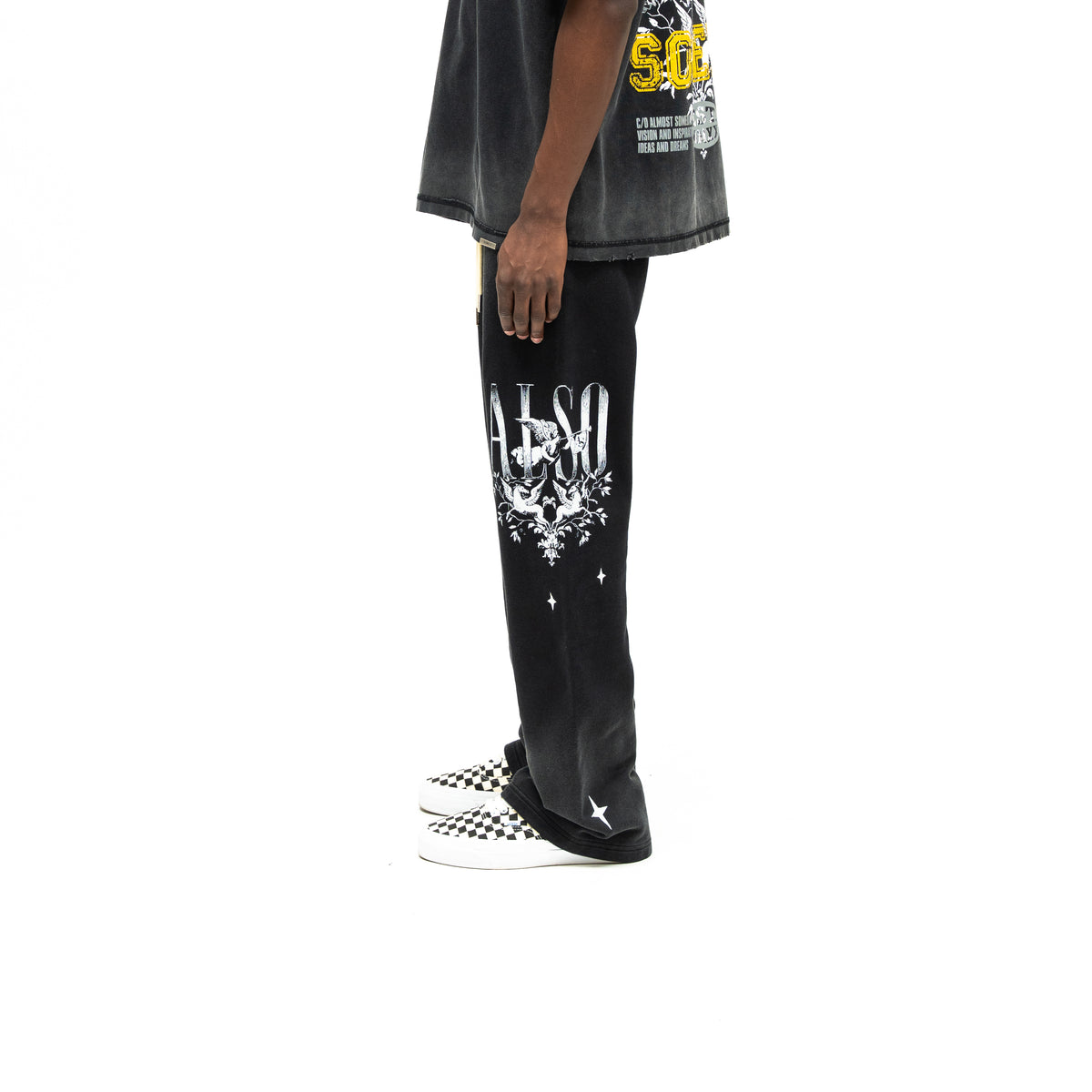 League Flare Sweatpants – Black – Side view on model styled with a tee, showing white lettering, winged figures, and flared hem