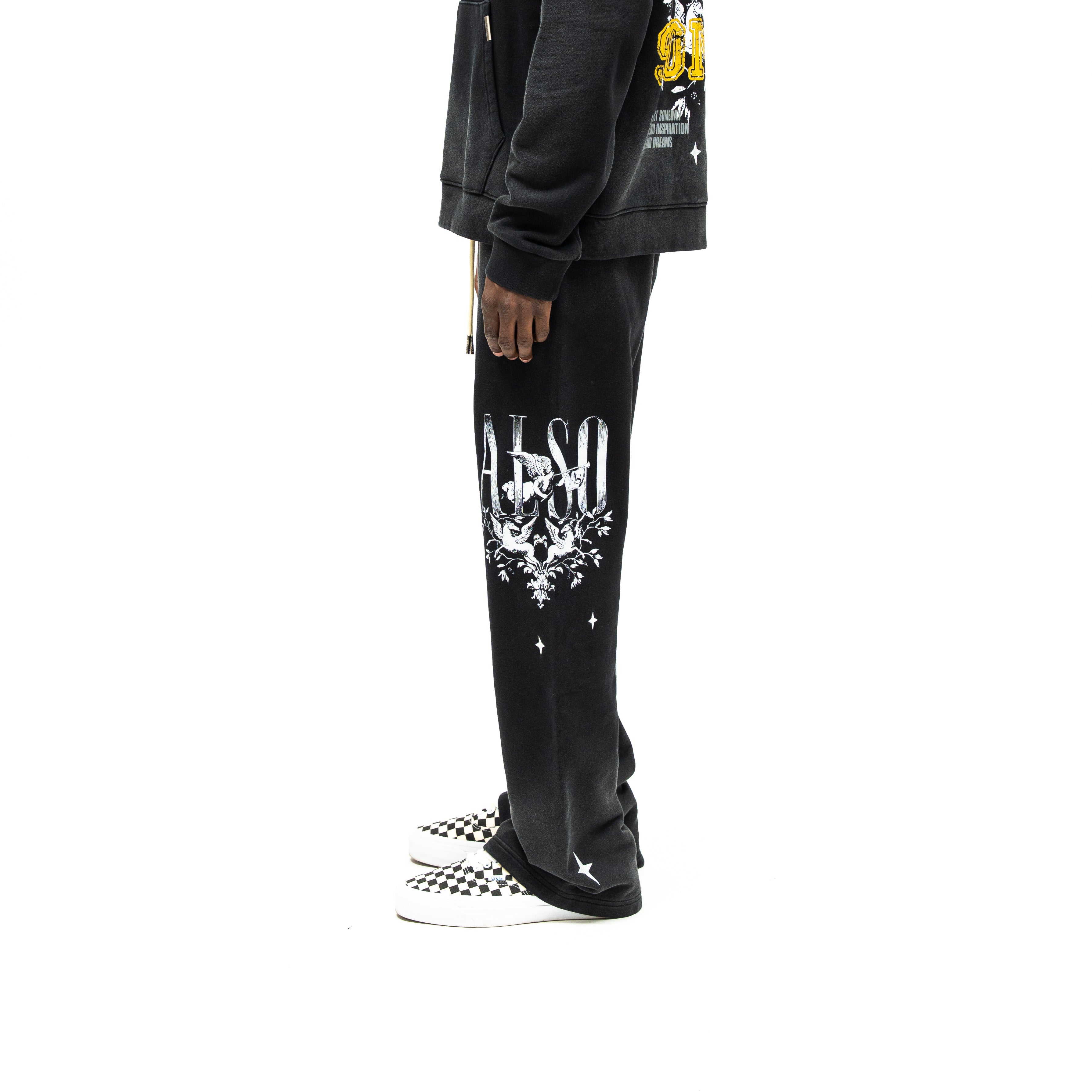 League Flare Sweatpants – Black – Side view on model styled with a hoodie, showing flared sweatpants with white lettering, winged figures, and stars