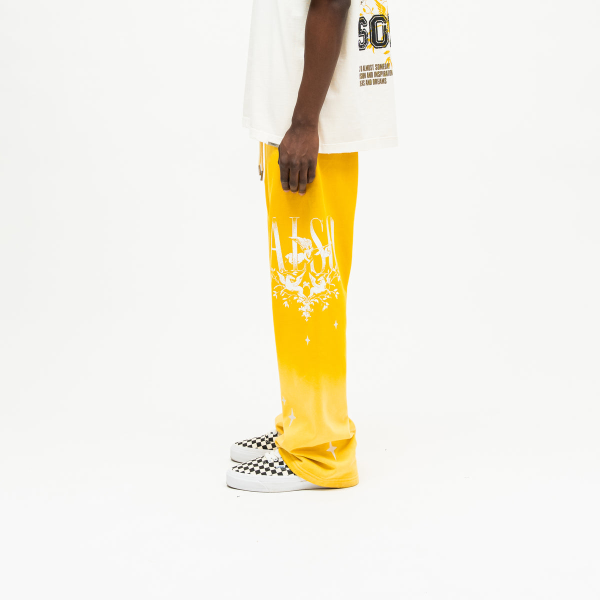 League Flare Sweatpants – Yellow – Side view on model styled with a cream tee, showing white lettering, winged figures, and flared hem