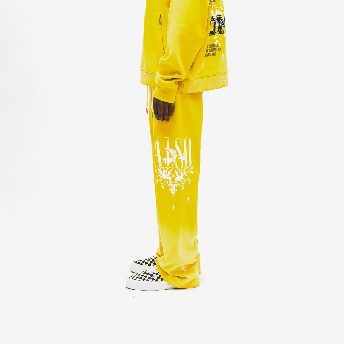League Flare Sweatpants – Yellow – Side view on model styled with a matching hoodie, showing flared sweatpants with white lettering, winged figures, and stars