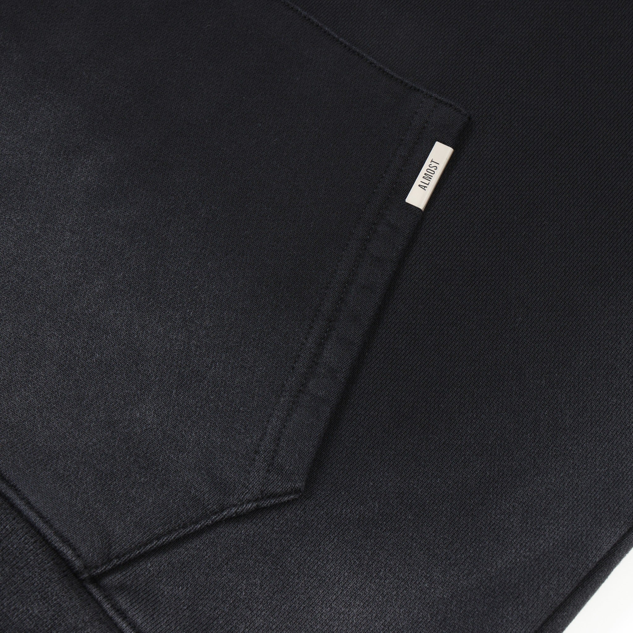 League Hoodie – Black – Close-up of kangaroo pocket with metal ALMOST logo tab