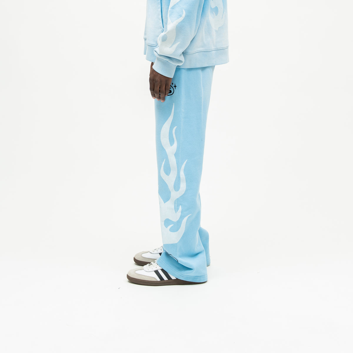Members Flare Sweatpants – Light Blue – Side view on model showing black thigh logo, white flames down outer leg, and flared hem