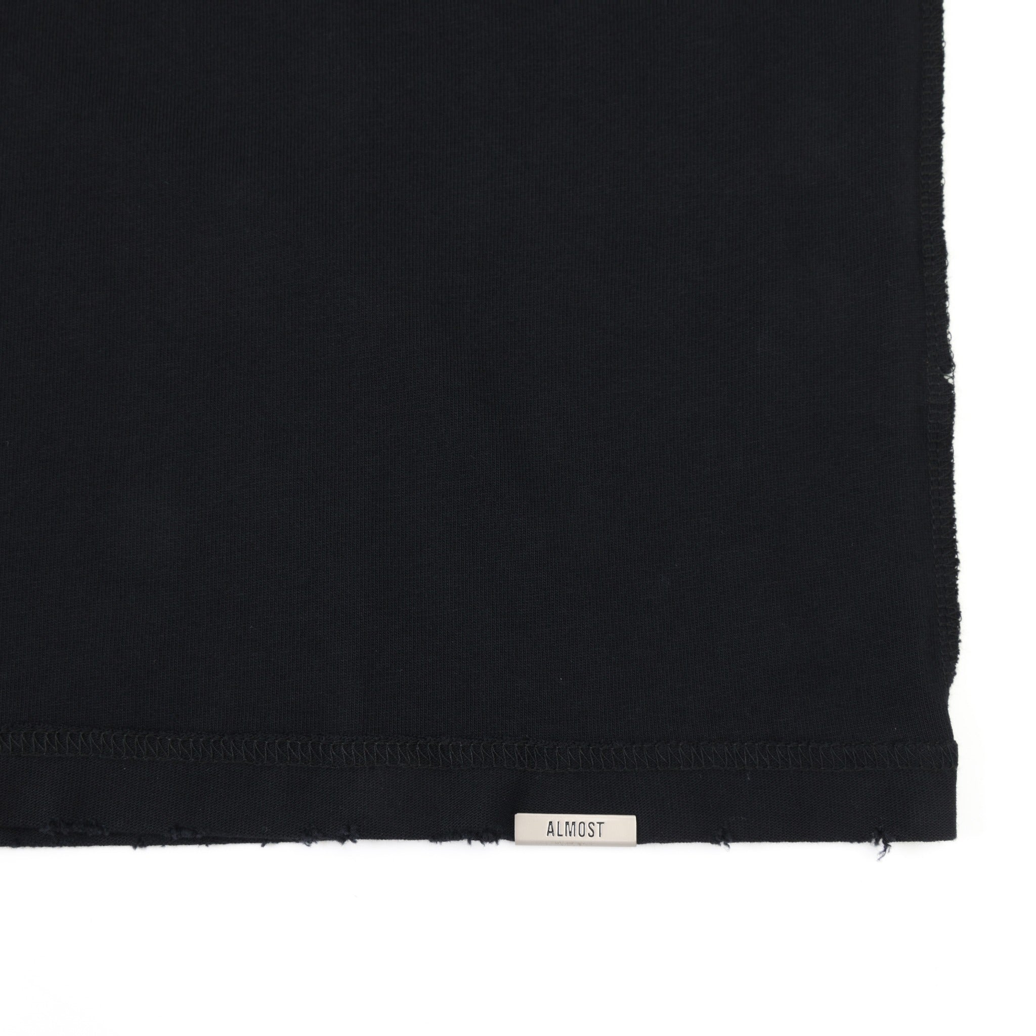 Members Tee – Black – Close-up of metal ALMOST logo at the distressed bottom hem