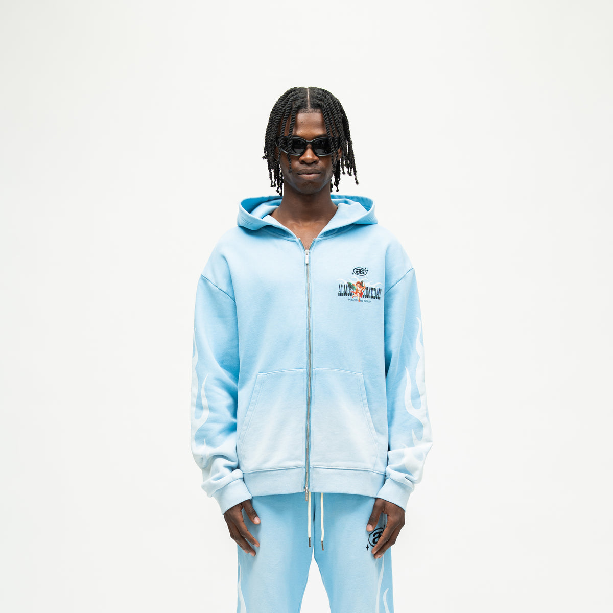 Members Zip Hoodie – Light Blue – Front view on model showing zip closure, chest graphic, front pockets, and white sleeve flames