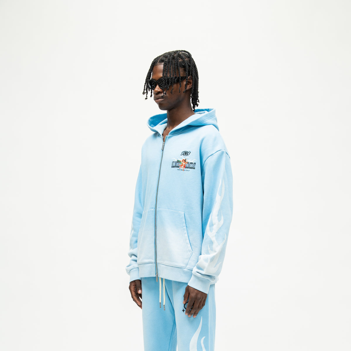 Members Zip Hoodie – Light Blue – Three-quarter front view on model showing chest artwork, dropped shoulders, and white sleeve flames