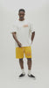 A video of a man wearing a cream-colored graphic t-shirt with a large back print and yellow pants, set against a plain light gray studio background.