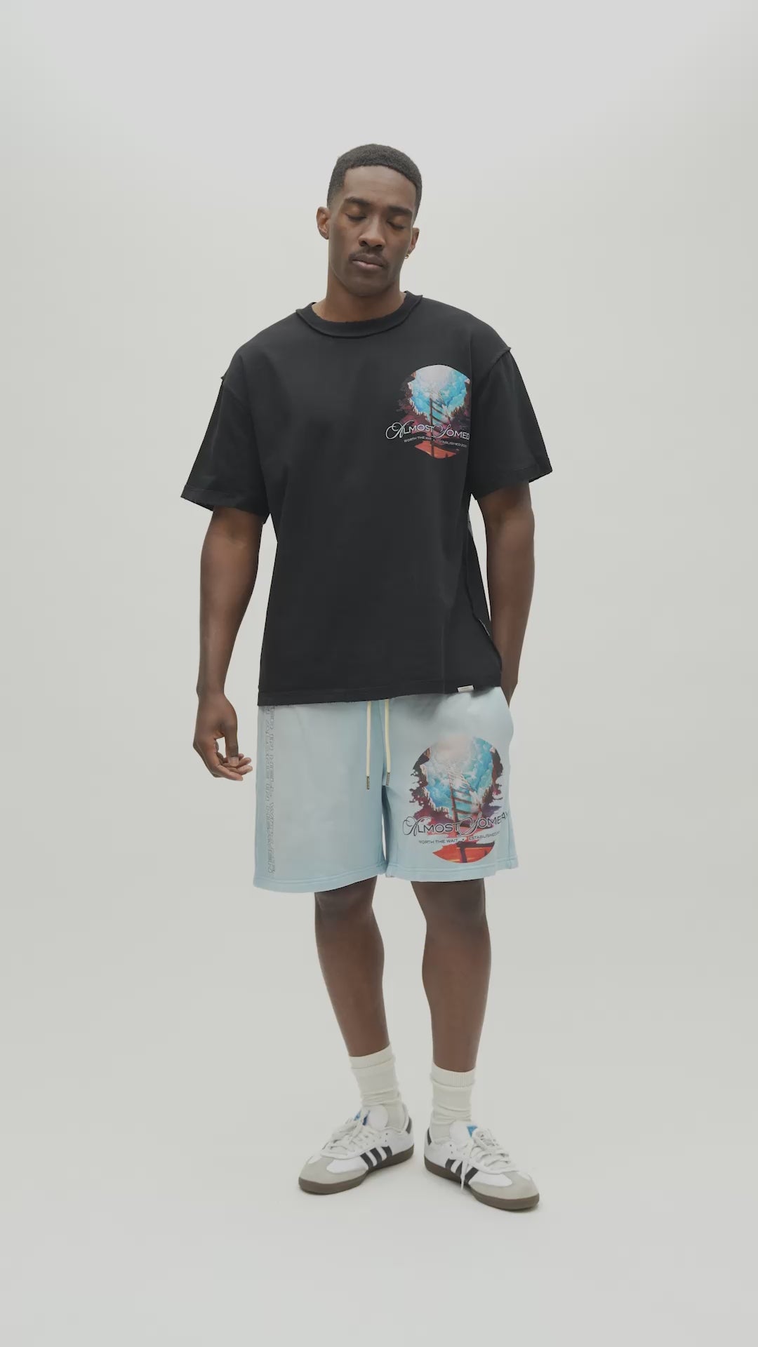 A man wearing a black t-shirt with a large colorful graphic print on the back, along with light blue sweatshorts.