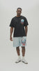 A man wearing a black t-shirt with a large colorful graphic print on the back, along with light blue sweatshorts.