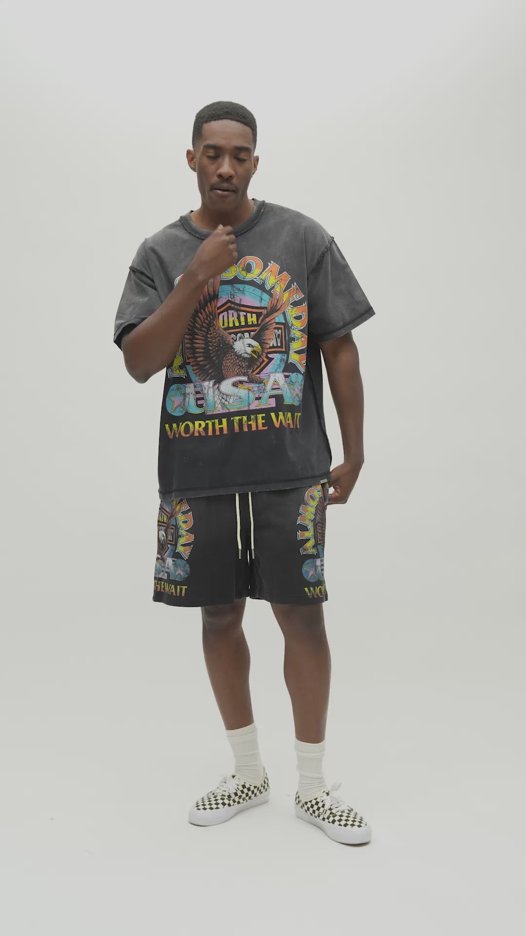 A man wearing a dark gray acid-wash graphic t-shirt with a colorful front print that reads 'ALMOST SOMEDAY' and 'WORTH THE WAIT', paired with matching dark gray sweatshorts, against a plain light gray background.