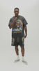 A man wearing a dark gray acid-wash graphic t-shirt with a colorful front print that reads 'ALMOST SOMEDAY' and 'WORTH THE WAIT', paired with matching dark gray sweatshorts, against a plain light gray background.