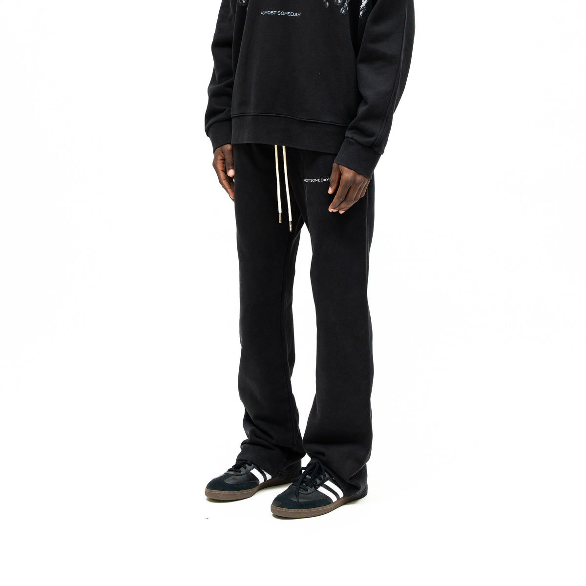 Smoke Flare Bottoms – Black – Three-quarter front view on model styled with black crewneck, showing drawstrings and flared leg openings