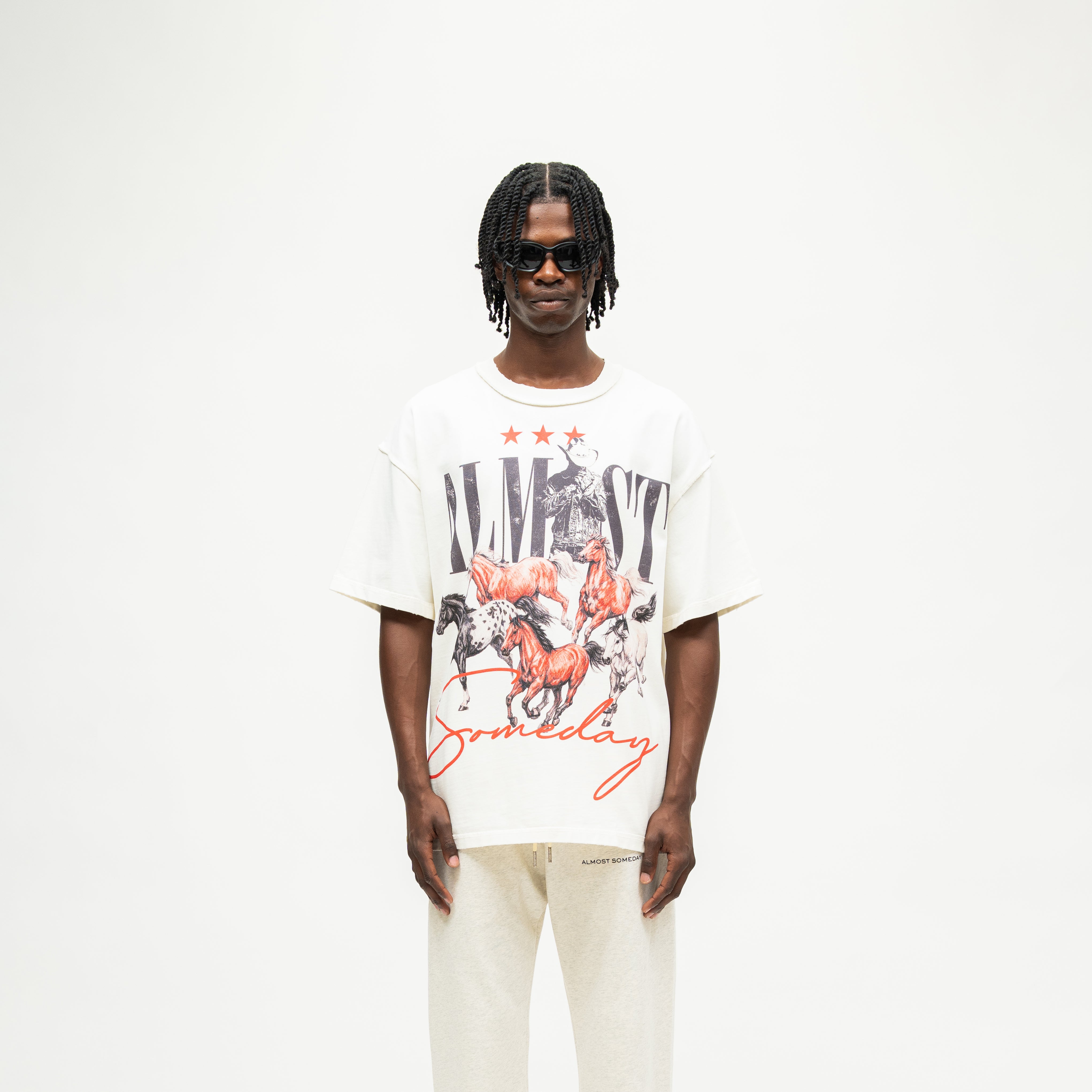 Smoke Tee – Cream – Front view on model showing cowboy and running horses graphic with black Almost lettering and red Someday script