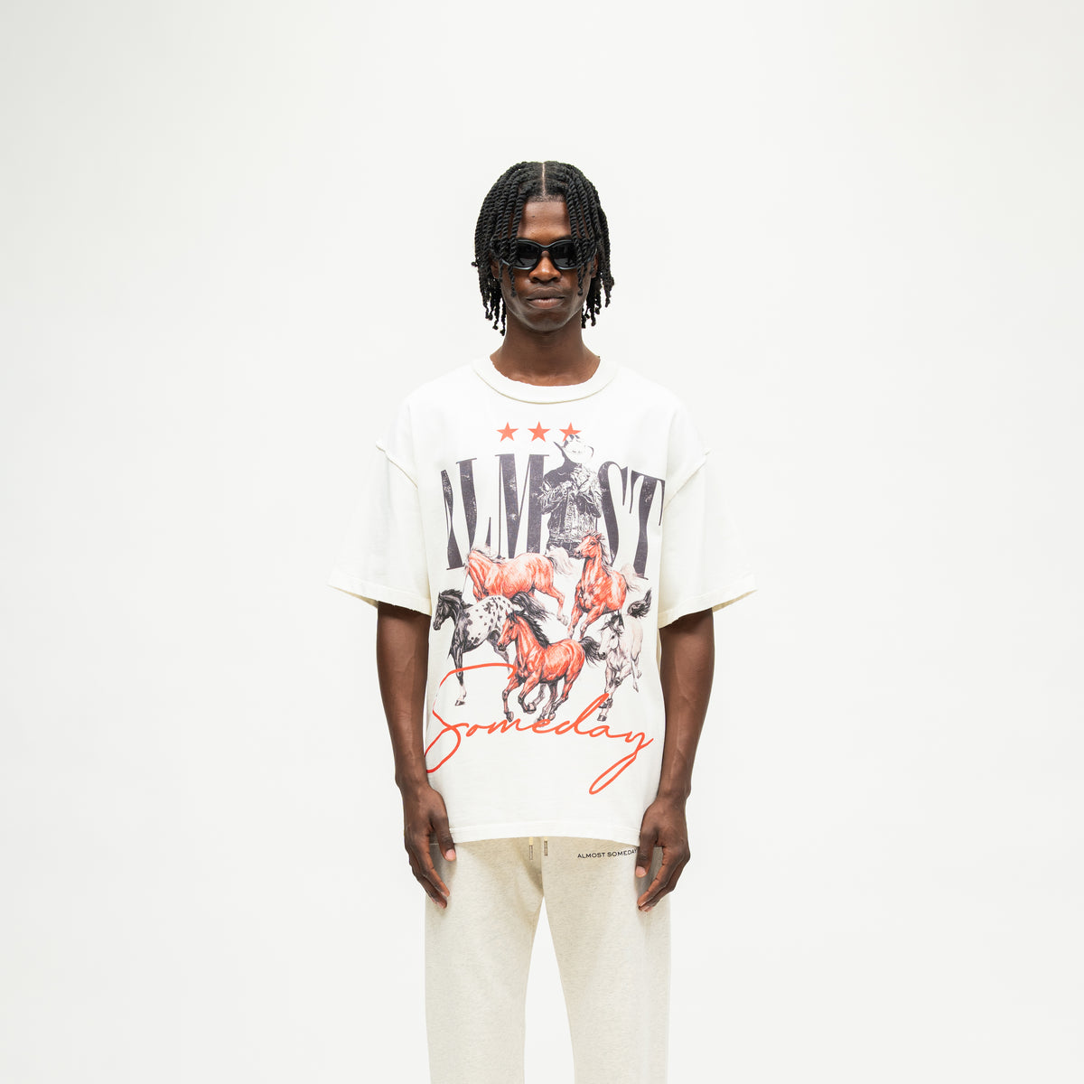 Smoke Tee – Cream – Front view on model showing cowboy and running horses graphic with black Almost lettering and red Someday script