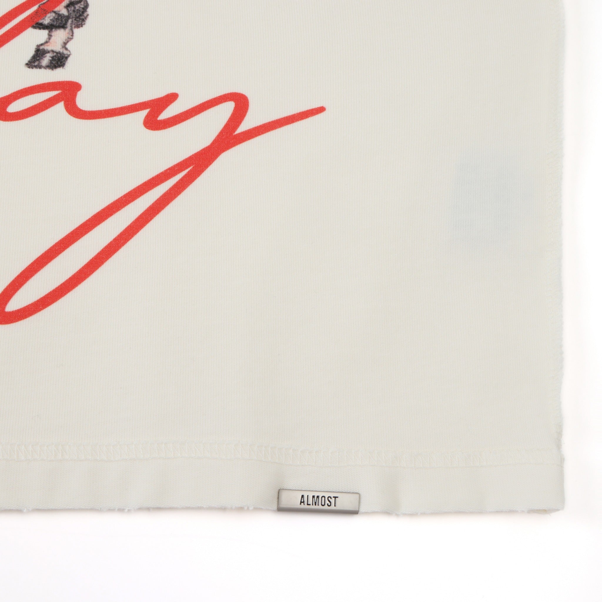 Smoke Tee – Cream – Close-up of lower hem with Almost label and red script detail
