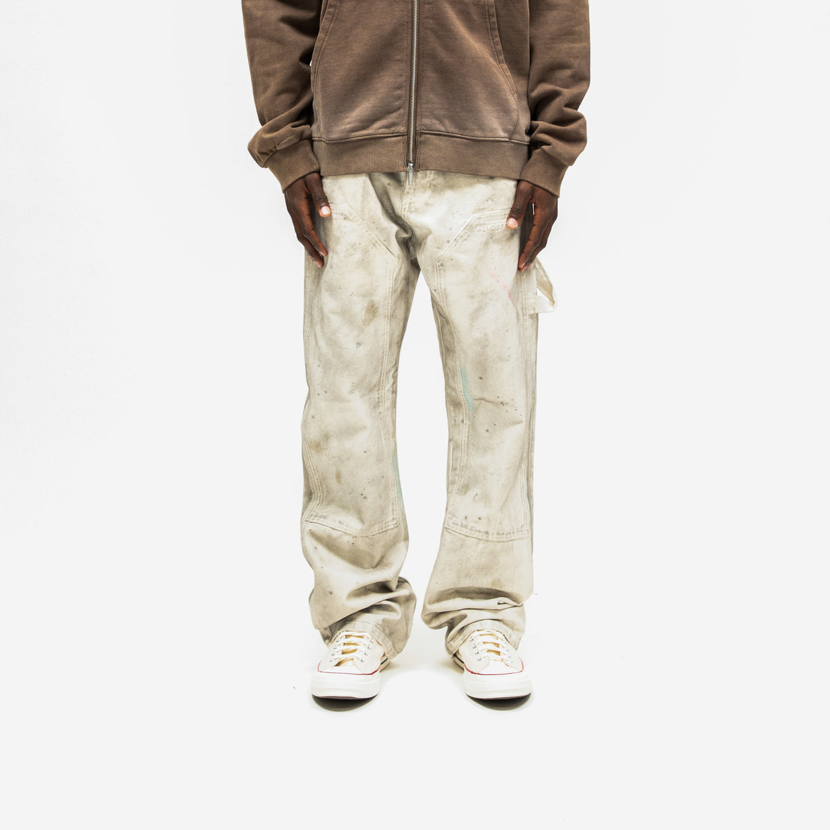 Spade Pants – Cream – Front view on model styled with brown zip hoodie, showing stitched thigh panels and mottled finish
